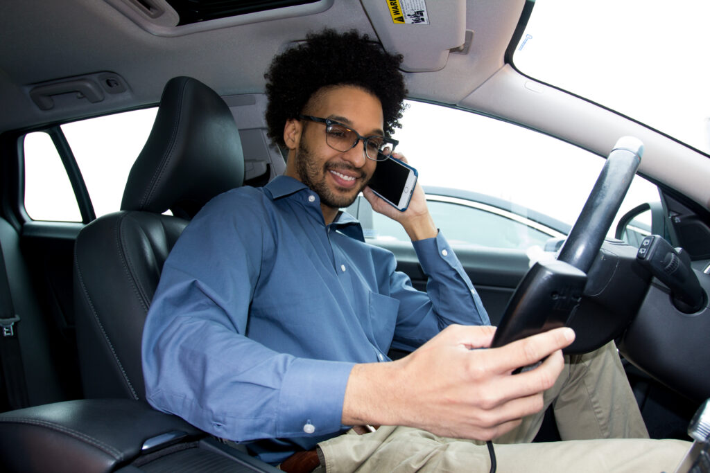 Man on phone in car smiling looking down at interlock device in hand